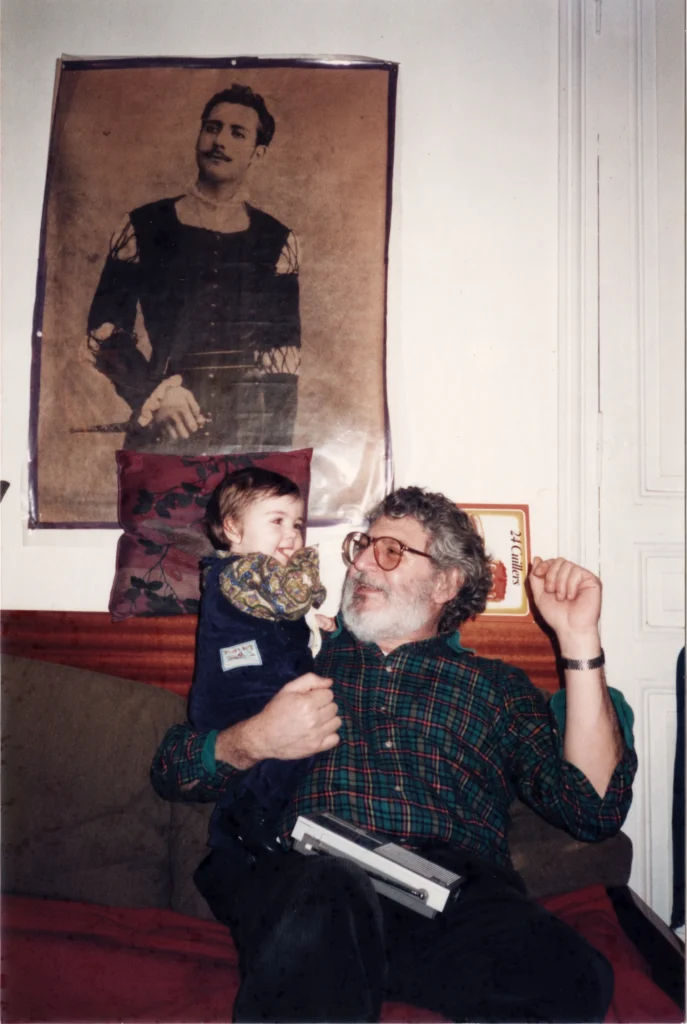 A young Miléna Kartowski-Aïach is held by her beaming father, Pierre Aïach, in front of the treasured portrait of her great-grandfather, Élie Léon Lévi-Valensin